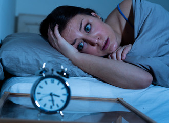 Attractive woman in bed staring at alarm clock trying to sleep feeling stressed and sleepless