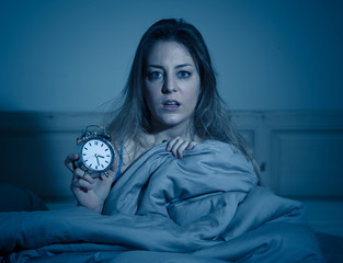 Attractive woman in bed showing alarm clock to camera feeling worried, stressed and sleepless