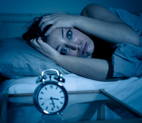 Attractive woman in bed staring at alarm clock trying to sleep feeling stressed and sleepless