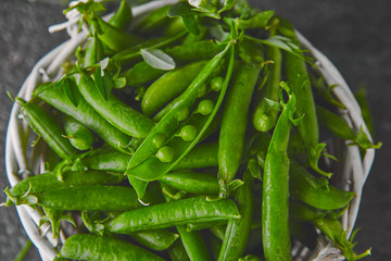 White Basket with fresh green peas on black background. Vegan and vegetarian food concept. Flat lay.