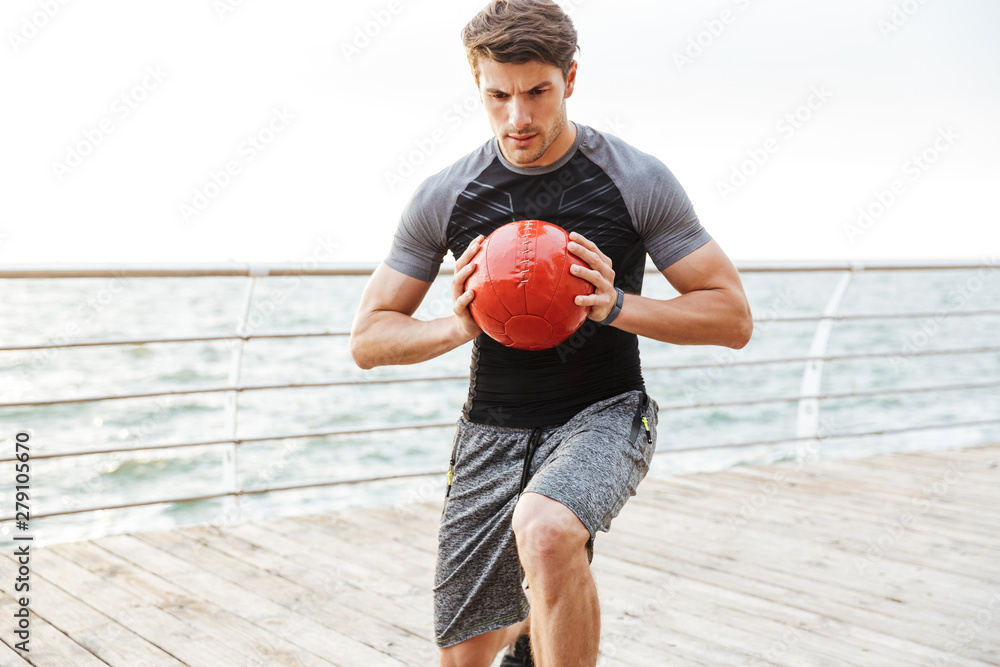 Sticker Strong serious concentrated young sports man outdoors make exercises with ball.