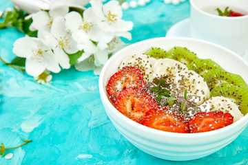 Healthy breakfast bowl smoothie with strawberry, banana, kiwi  and chia seeds on blue background. Healthy vegan food concept..