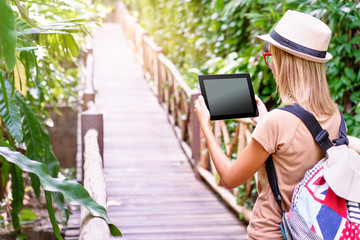 Fototapeta premium Travelling concept. Technology and adventure. Young woman using tablet computer in jungle.