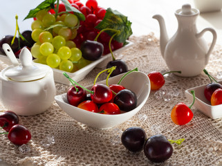 Fruits for breakfast. Healthy food. Нealthy lifestyle. Vegan food. Vegan diet. Red and green bunches of grapes, cherry lie on a white dish. The light from the window falls beautifully on the fruit pla