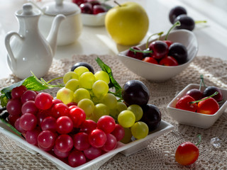 Fruits for breakfast. Healthy food. Нealthy lifestyle. Vegan food. Vegan diet. Red and green bunches of grapes, cherry, apple lie on a white dish. The light from the window falls beautifully on the fr