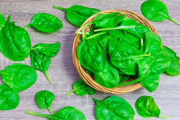 Small juicy green spinach leaves in wicker bowl and on wooden table