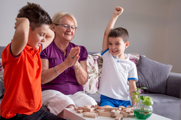 Two boys with grandmother playing game at home, Happy kids playing with senior woman at home....