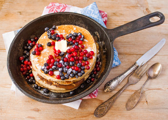 Homemade pancakes on a black cast iron skillet with berries on wooden background vintage tableware