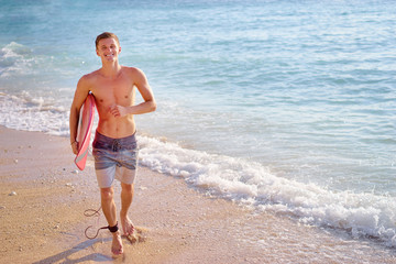 Naklejka na ściany i meble Hobby and vacation. Holiday on the beach. Young man carrying surf board.