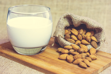 Ripe unpeeled almonds in a hemp sack and almond milk in a glass on a wooden cutting board. Food photography. Minimalist photography.