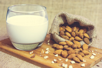 Ripe unpeeled almonds in a hemp sack and almond milk in a glass on a wooden cutting board. Food photography. Minimalist photography.