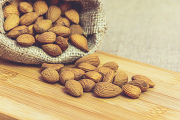 Ripe unpeeled almonds in jute bag on wooden board. Food photography. Minimalist photography.