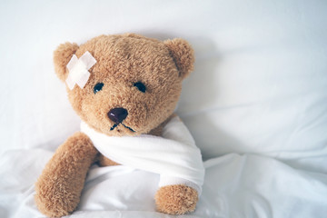 Teddy bear lying sick in bed With a headband and a cloth covered