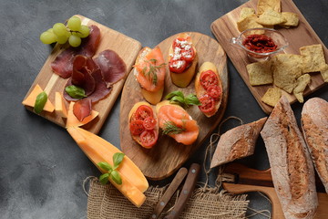 Brushetta or traditional Spanish tapas. Appetizers with Italian antipasti snacks. Variety of small sandwiches with cherry tomatoes, salmon, cream cheese. Prosciutto served with melon and basil