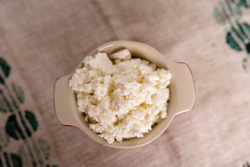 dairy product cottage cheese in brown ceramic bowl with spoon on vintage wooden table