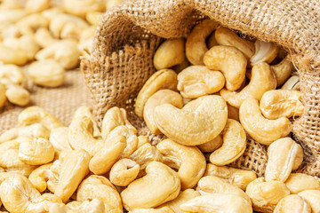 Detail on a healthy cashew nuts spilled from a hemp sack and on a burlap background. Food photography. Healthy fresh cashew nuts. The Latin name of cashew is Anacardium occidentale.