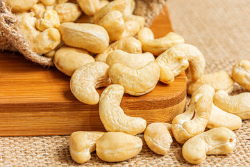 Detail on a healthy cashew nuts spilled from a hemp sack and on a burlap background. Food photography. Healthy fresh cashew nuts. The Latin name of cashew is Anacardium occidentale.