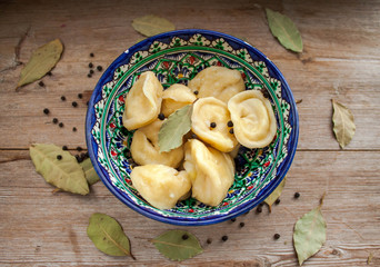 Dumplings with potato or meet served with butter or sour cream in dish on rustic wooden background