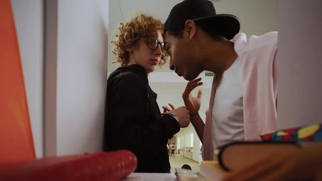 Portrait of a tender boy student opens his locker to prepare for classes. Rude afro classmate pushes him and takes his power bank without a request.