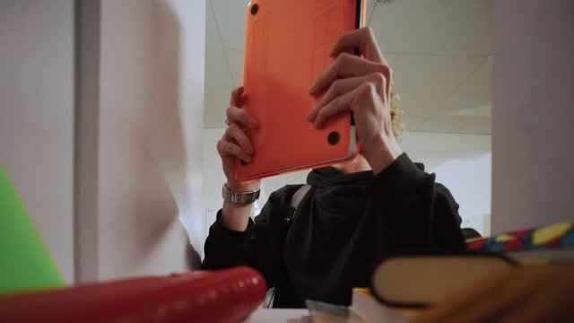 Funny scene inside a student locker in school. Portrait of a silly curly-haired guy stealing his friend's laptop and nunchaku for a joke.