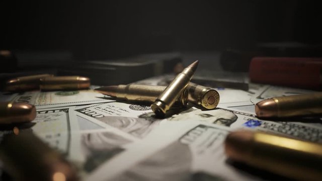 Small pile of ammo bullets on a table covered with countless dollar bills. 4KHD