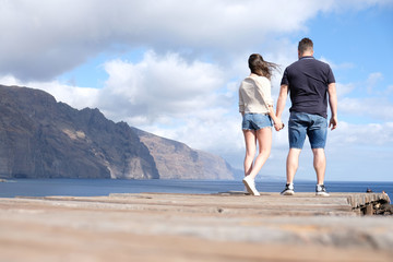 Low angle view of a young couple holding hands with cliffs, cloudy sky and the sea in the background