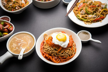 Assorted Indo chinese food in group includes non vegetarian or chicken Schezwan/Szechuan hakka noodles, fried rice, manchurian, egg american chop suey, soup with spoon and chop sticks, selective focus