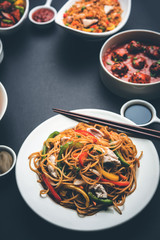 Assorted Indo chinese food in group includes non vegetarian or chicken Schezwan/Szechuan hakka noodles, fried rice, manchurian, egg american chop suey, soup with spoon and chop sticks, selective focus