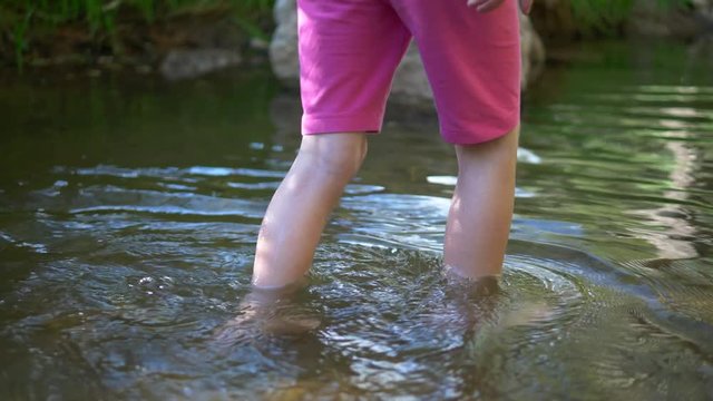 A little girl wading in a river in the forest.