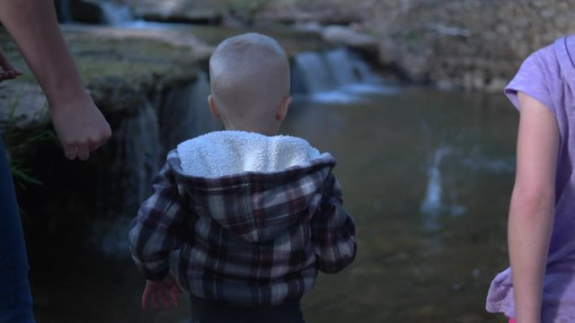 Young boy throwing rocks into a river with his family cheering him on.