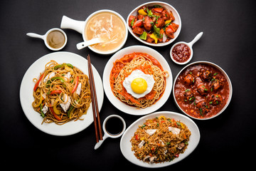 Assorted Indo chinese food in group includes non vegetarian or chicken Schezwan/Szechuan hakka noodles, fried rice, manchurian, egg american chop suey, soup with spoon and chop sticks, selective focus
