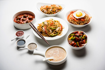 Assorted Indo chinese food in group includes non vegetarian or chicken Schezwan/Szechuan hakka noodles, fried rice, manchurian, egg american chop suey, soup with spoon and chop sticks, selective focus