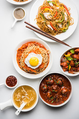 Assorted Indo chinese food in group includes non vegetarian or chicken Schezwan/Szechuan hakka noodles, fried rice, manchurian, egg american chop suey, soup with spoon and chop sticks, selective focus