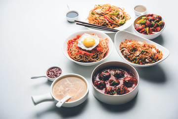 Assorted Indo chinese food in group includes non vegetarian or chicken Schezwan/Szechuan hakka noodles, fried rice, manchurian, egg american chop suey, soup with spoon and chop sticks, selective focus