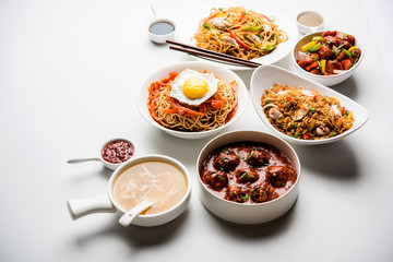 Assorted Indo chinese food in group includes non vegetarian or chicken Schezwan/Szechuan hakka noodles, fried rice, manchurian, egg american chop suey, soup with spoon and chop sticks, selective focus