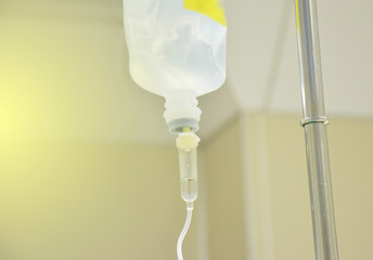 The saline solution bag is hung with pole. The bag connect with intravenous (IV) set is giving to patient. There is yellow gradient at left. There is copy space for texture.