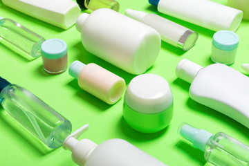 Close-up set of diffrent sized bottles and jars for cosmetic products on green backgound. Face and body care concept with copy space