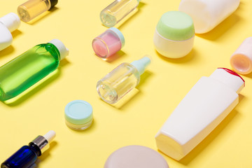 Composition of different sized cosmetic jars and bottles on yellow background. Beauty care concept with copy space