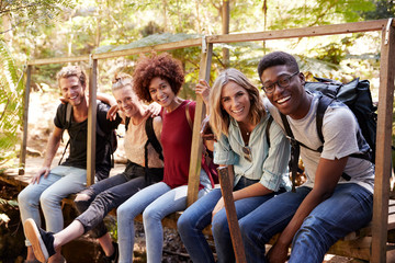 Five young adult friends on a hike sitting together laughing to camera during a break, close up
