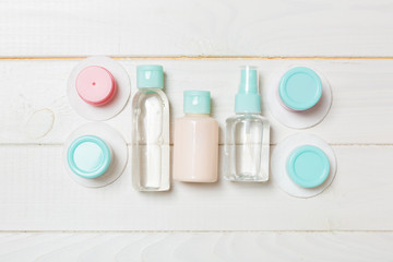 Set of travel size cosmetic bottles on white wooden background. Flat lay of cream jars. Top view of bodycare style concept