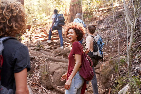 Group of millennial  friends hiking uphill on a forest trail, three quarter length