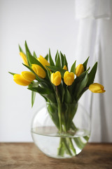 A bouquet of yellow tulips in a vase on the windowsill. A gift to a woman's day from yellow tulip flowers. Beautiful yellow flowers in a vase by window.