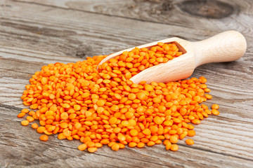 Photo of red lentils in wooden bowl with spoon on wooden background. Product photo of red lentils. Healthy lifestyle. Vegetarian and vegan diet. Spilled lens