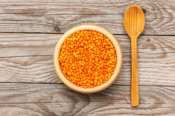 Flat lay photo of red lentils in wooden bowl with spoon on wooden background. Product photo of red lentils. Healthy lifestyle. Vegetarian and vegan diet. Spilled lens