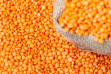 Red lentils in a sack cloth. Product photo of red lentils. Healthy lifestyle. Vegetarian and vegan diet. Spilled lens