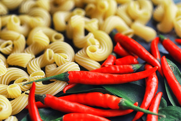Uncooked pasta on a stone background. With seasonings and spices, spicy chili peppers.