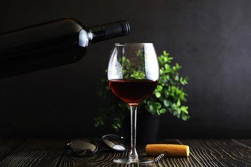 A glass of red dry wine on the table. Dark bottle and glass of wine.