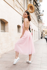 Photo of pleased young woman wearing summer dress and straw hat walking on city street