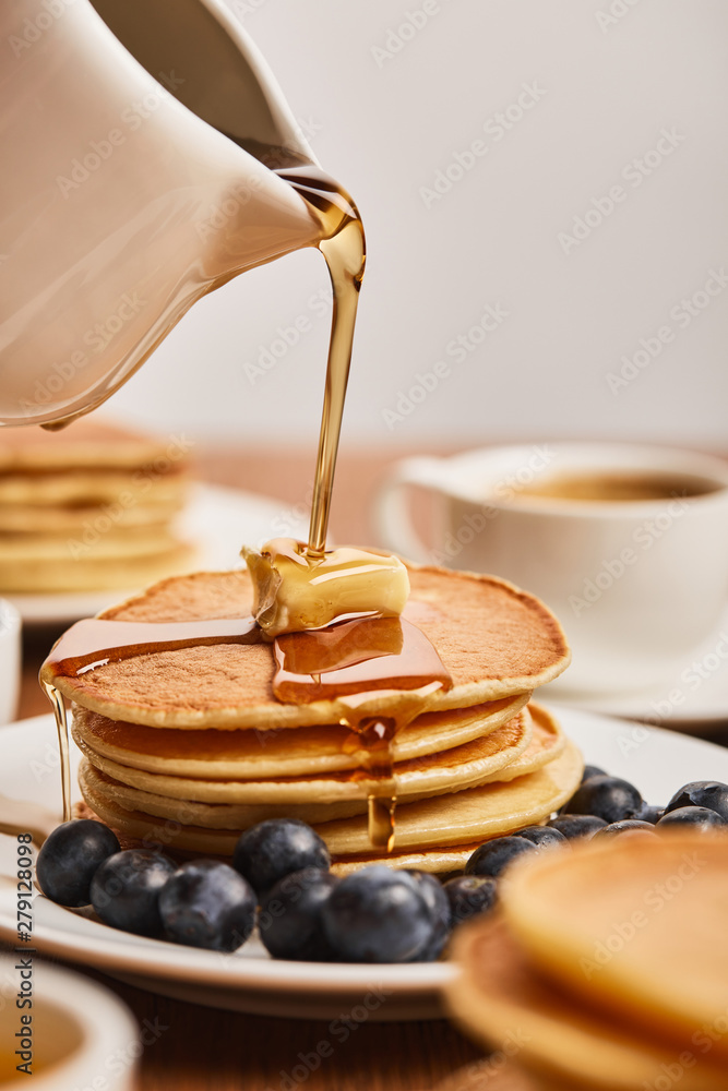 Wall mural selective focus of syrup pouring on pancakes with butter and blueberries near cup of coffee