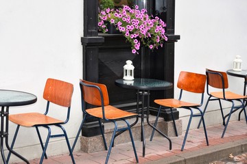 Empty design street cafe with white flashlight with a candle on the table and cozy wooden chairs. Beautiful elegant restaurant on paved street in the old town with pink petunia flowers on background